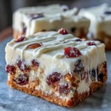 Frosted Cranberry Bliss Bars are cut into squares, scattered with white chocolate drizzle and extra dried cranberries.