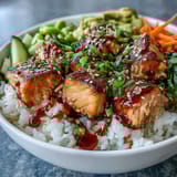 Vibrant Baked Salmon Rice Bowl topped with shredded carrots and edamame, drizzled with spicy sriracha mayo.