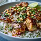 Vibrant Peanut Chicken Protein Bowl with sautéed chicken over coconut rice, topped with crisp red cabbage and carrots, drizzled with creamy peanut sauce.