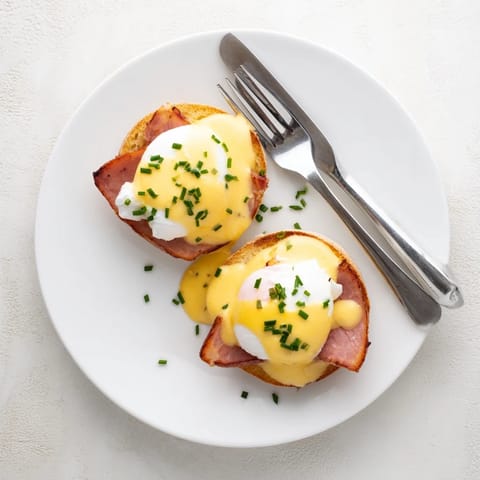 Eggs Benedict breakfast plate garnished with chives beside a mimosa for weekend brunch.