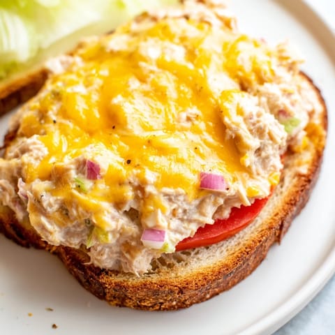 A close-up of a hot Tuna Melt with melted cheese oozing over creamy tuna salad.