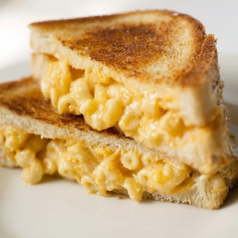 A skillet holds a hot mac & cheese grilled cheese sandwich, served alongside a comforting bowl of tomato soup.