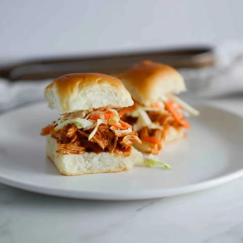 Golden BBQ chicken sliders on toasted mini buns with creamy, crunchy slaw on a platter.
