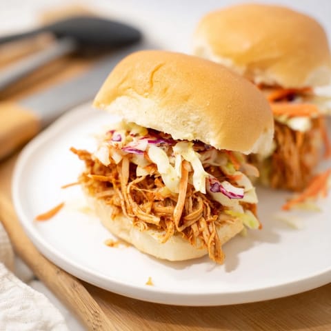 Mini buns packed with saucy pulled BBQ chicken and tangy coleslaw for a party.