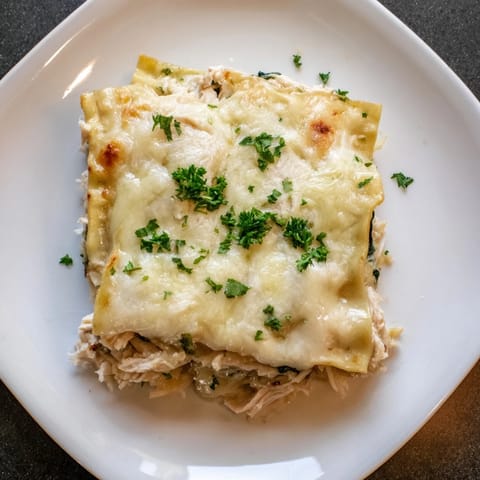 A close-up slice of creamy Chicken Alfredo Lasagna reveals tender chicken, spinach, and velvety Alfredo sauce between pasta sheets.