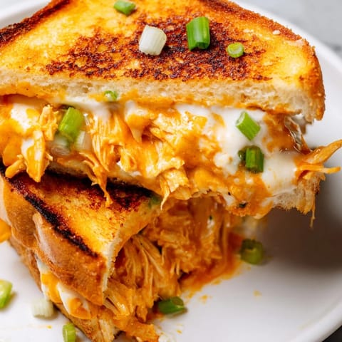 A close-up of a Buffalo Chicken Ranch Grilled Cheese cut in half, revealing juicy chicken, gooey cheese, and a crisp crust.