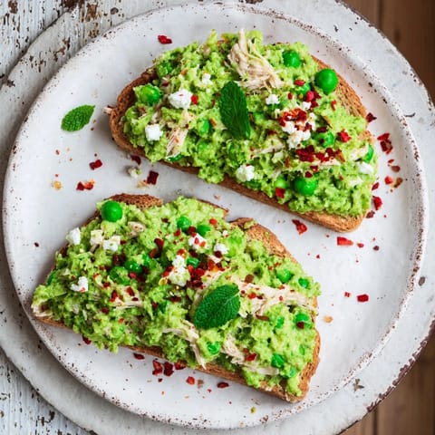 Golden-brown slices of Smashed Pea & Chicken Toast topped with fresh mint and a sprinkle of chili flakes, ready to serve.  