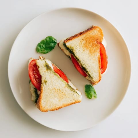 A vibrant Caprese Pesto Grilled Cheese sandwich features melted mozzarella and ripe tomato slices layered on sourdough, served warm beside a fresh basil garnish.