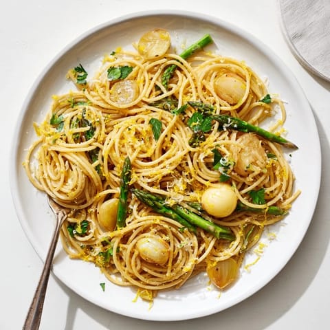 A close-up of Roasted Garlic & Asparagus Pasta, garnished with parsley, lemon zest, and grated Parmesan.