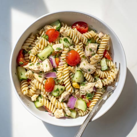 A vibrant bowl of Honey Mustard Chicken Pasta Salad served on a bed of greens, garnished with fresh parsley for a refreshing meal.