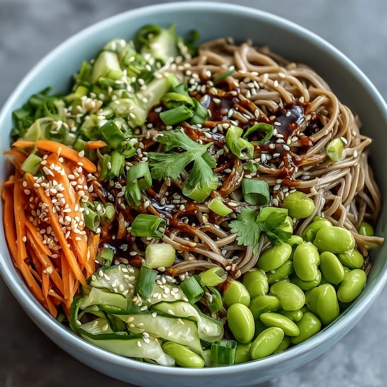 A vibrant serving of chilled Soba Noodle Bowl garnished with toasted sesame seeds and fresh cilantro, ready to be enjoyed with chopsticks.