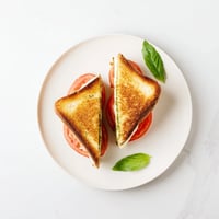 Golden, crispy sourdough slices are stuffed with melted mozzarella, juicy tomato rounds, and aromatic basil pesto in this Caprese Pesto Grilled Cheese.