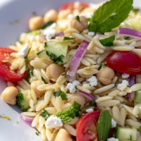A vibrant bowl of Lemony Chickpea Orzo Salad with chickpeas, cucumber, and feta on a rustic table.